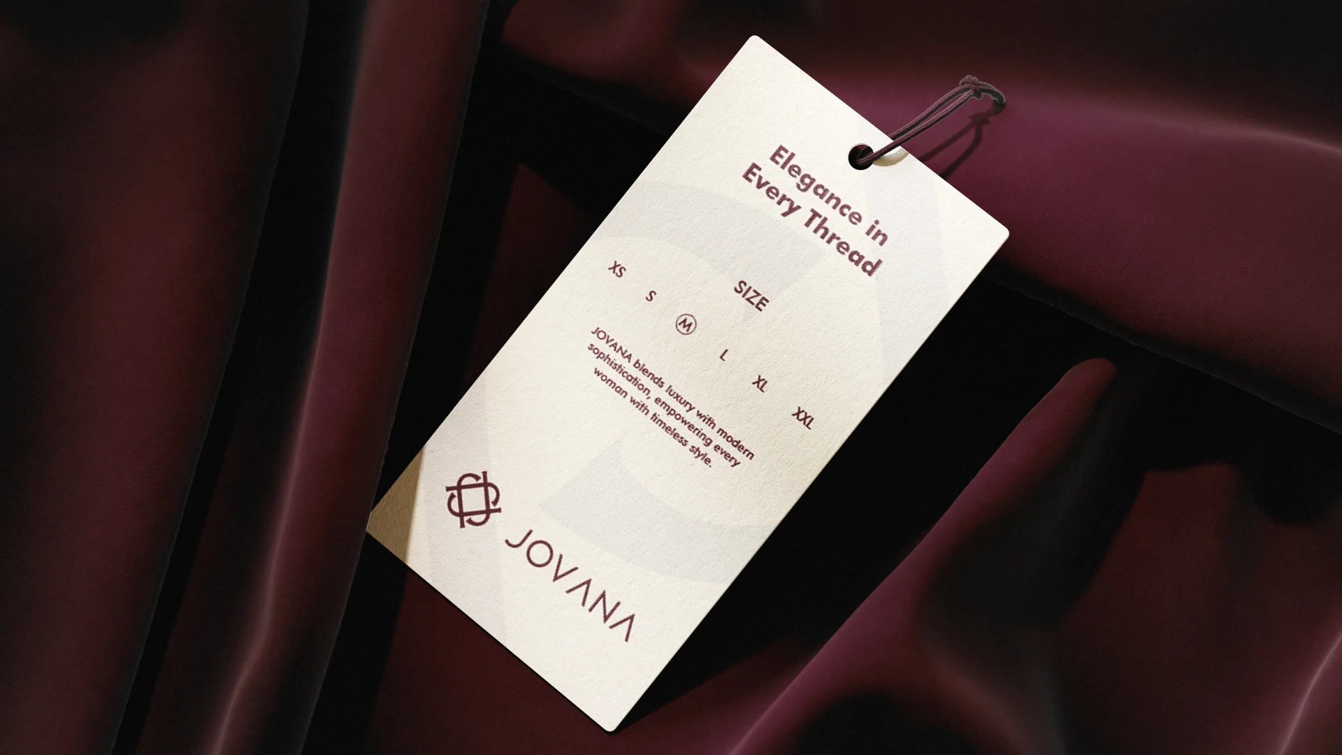 Jovana Elegance in Every Thread clothing hang tag on burgundy silk